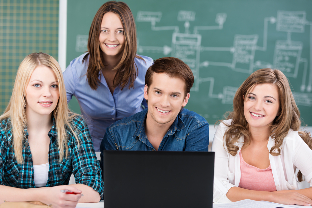 Attractive middle-aged woman teacher posing with a group of her teenage students in a college classroom