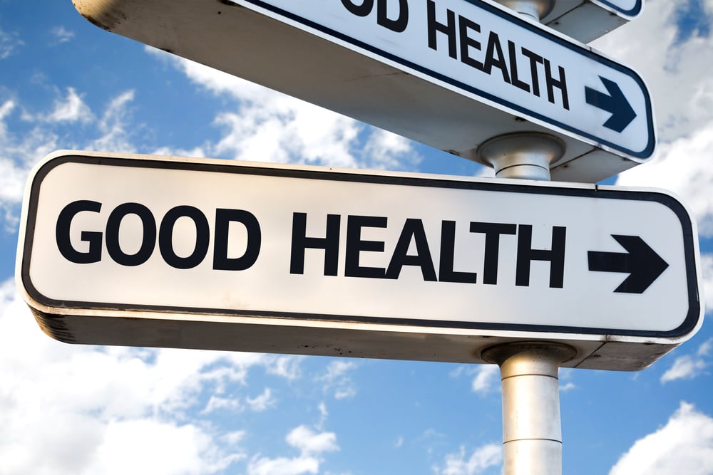 white sign with black border and capital black letters reading good health and arrow pointing right with blue sky and white clouds in background