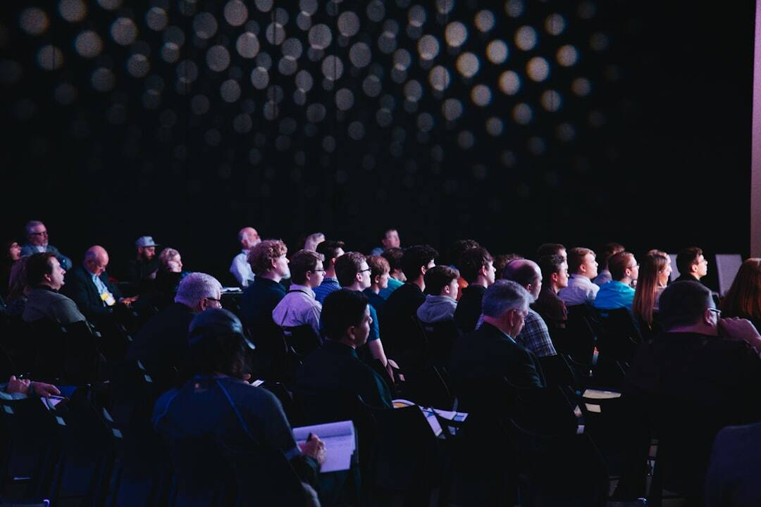 dark conference room with people sitting in chairs looking at stage