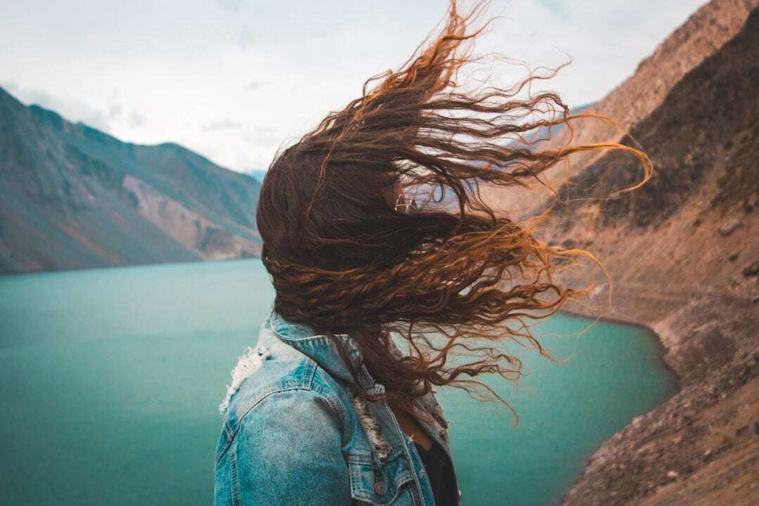 girl with hair blowing in wind with water and mountains in background
