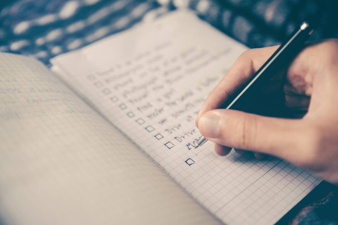 hand writing with a pen in a journal making a list with check boxes