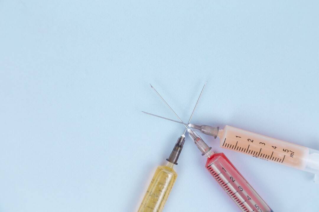 three syringes filled interesecting at the needles and each filled with different colors from left yellow, red and light orange