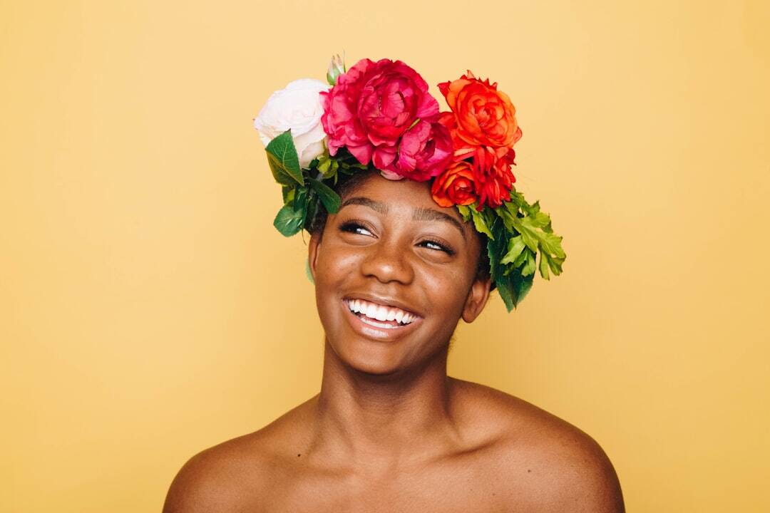 smiling skin of color woman with bright white pink orange and green flowers in her hair
