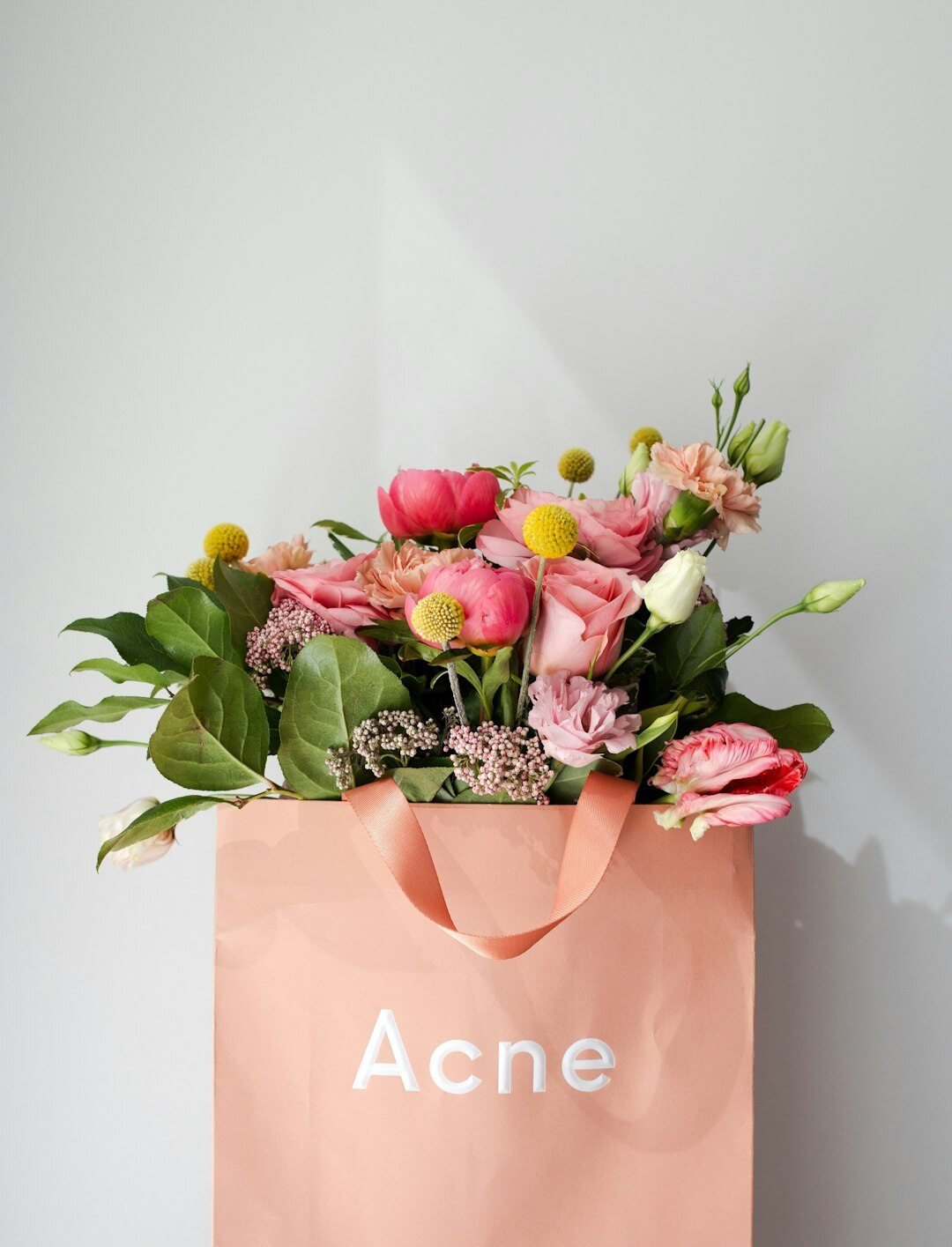 peach tote back with the word acne and filled with greenery and flowers. 