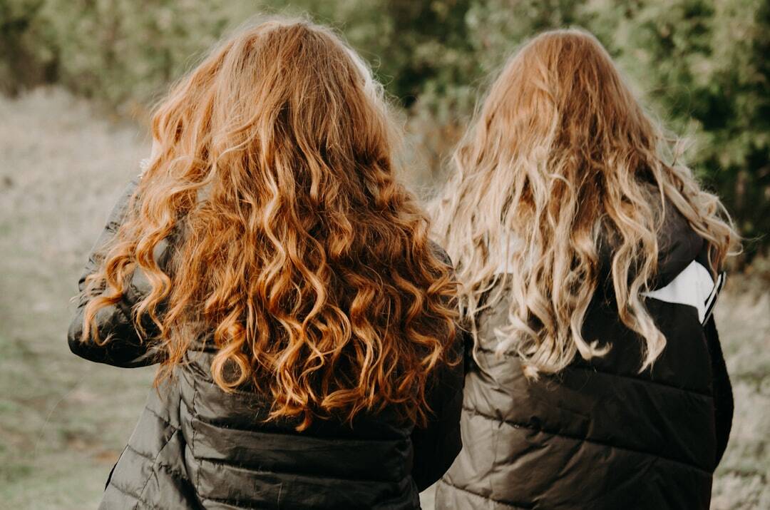 two children one with reddish brown curly hair and one with blonde curly hair sit facing away back to each other