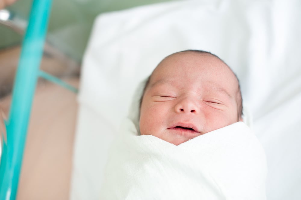 infant sleeping swaddled in white blanket on bed